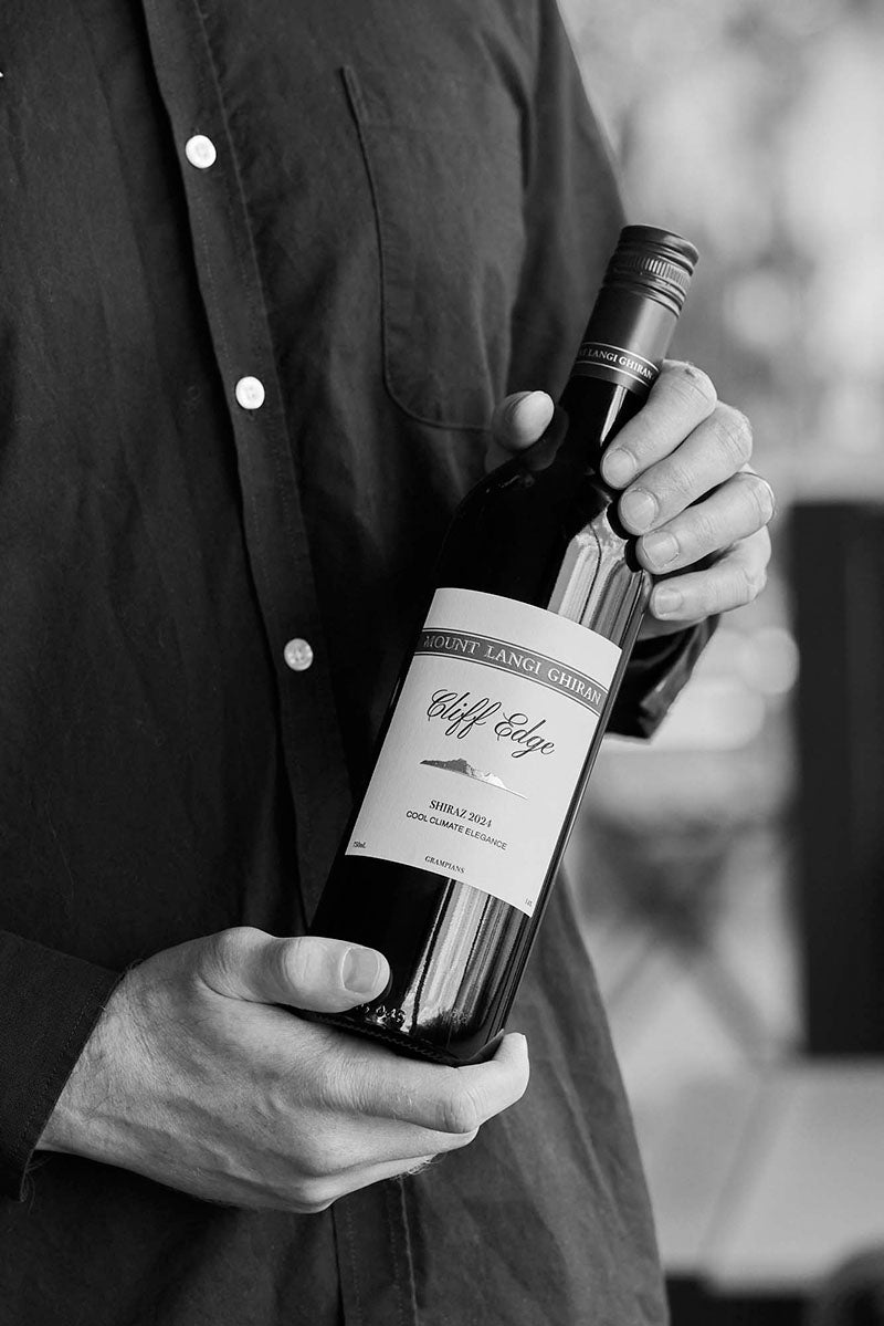 Black and white close-up of hands holding a bottle of Mount Langi Ghiran Cliff Edge Shiraz wine