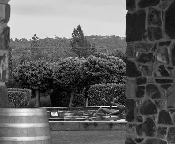 Black and white view of a swimming pool framed by stone pillars with people relaxing in the water
