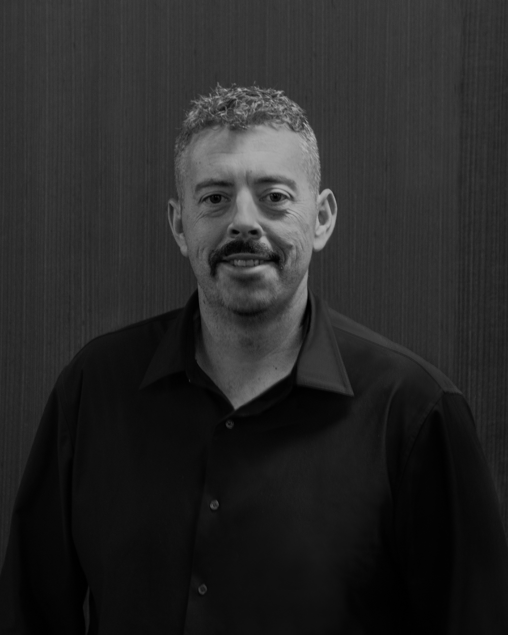 Black and white studio portrait of a smiling man with a moustache