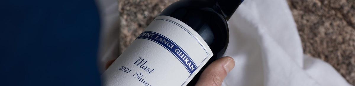 Close-up of a hand holding a Mount Langi Ghiran Mast 2021 Shiraz bottle, shop header banner
