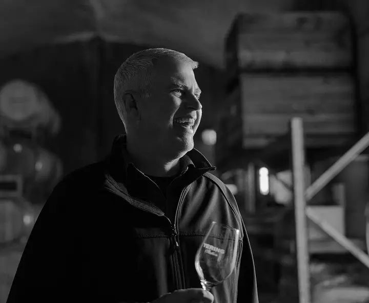 Black and white portrait of a winemaker smiling while holding a wine glass in the cellar