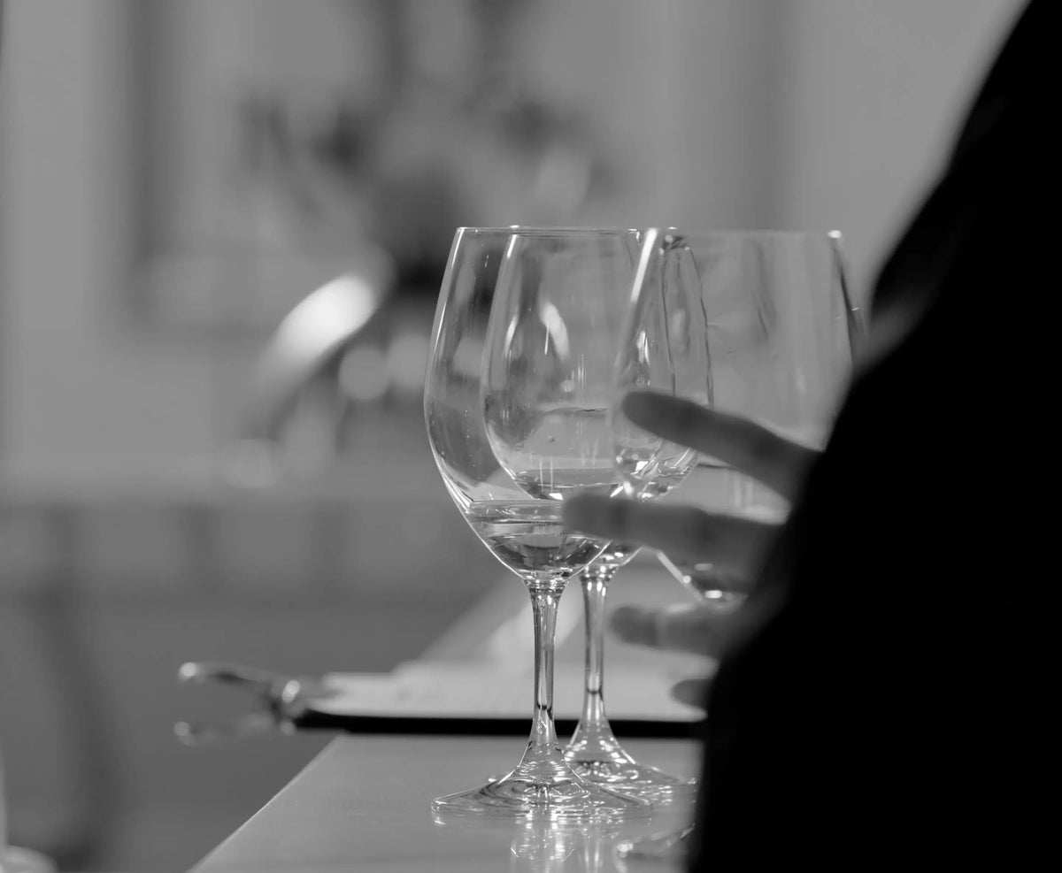 Black and white close-up of wine glasses on a bar with a hand reaching toward them