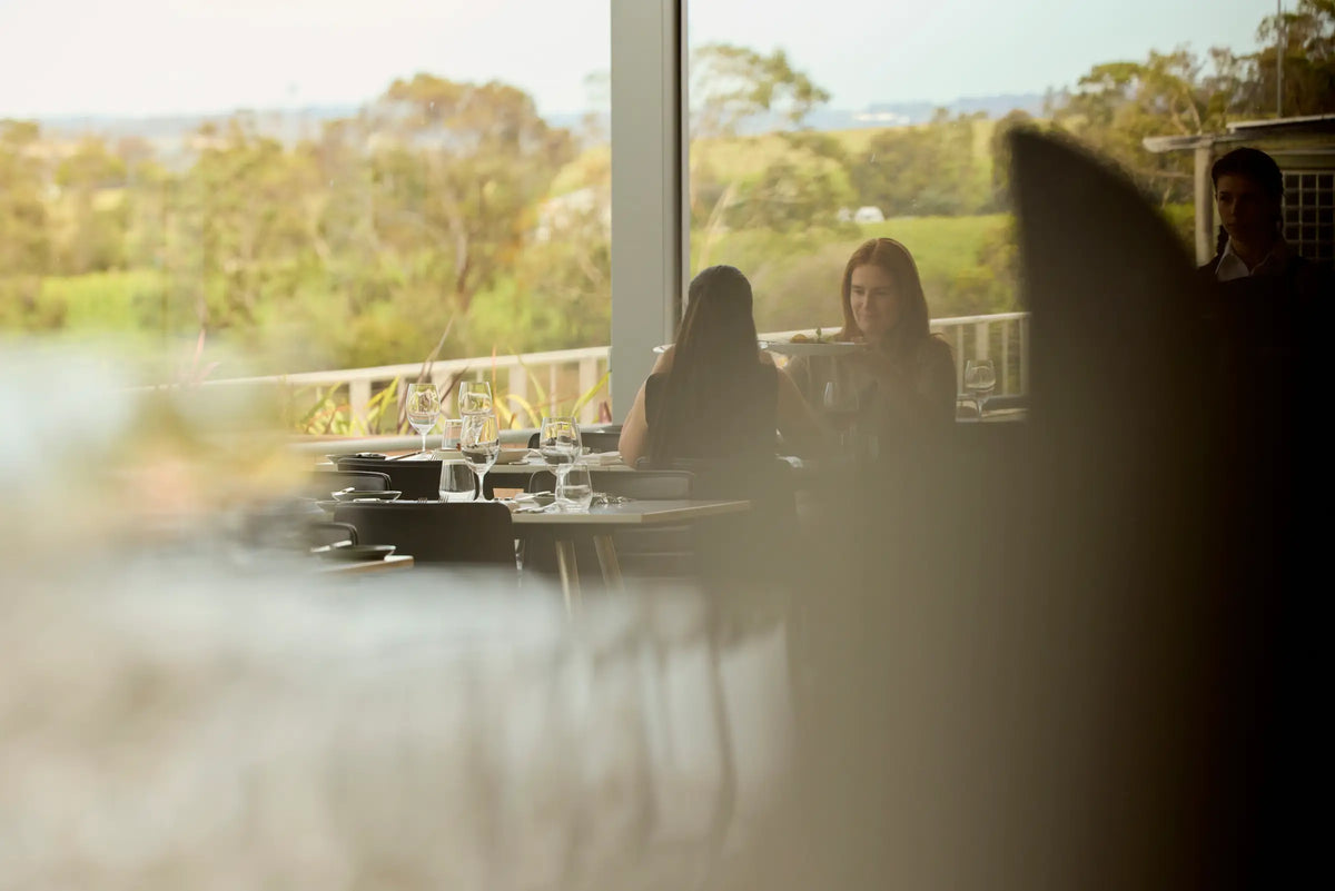 Diners at a restaurant table overlooking the vineyard through a large window