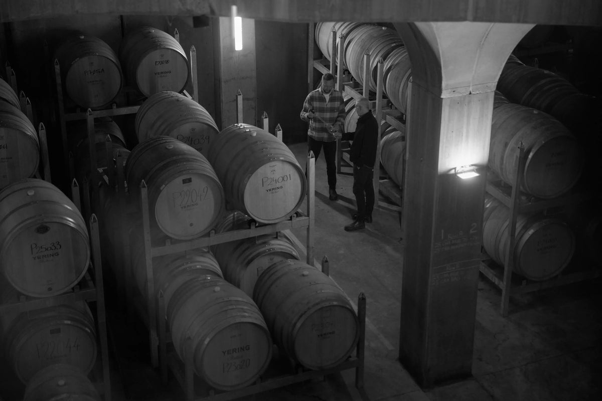 Black and white photo of two men examining wine barrels in the cellar