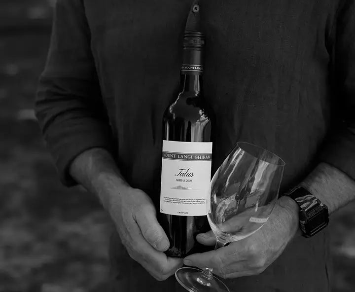 Black and white close-up of hands holding a bottle of Mount Langi Ghiran Talus Shiraz and a wine glass